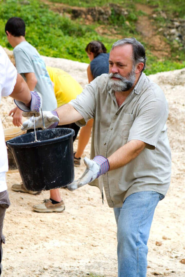 Man helps pass along a bucket of dirt to a fellow missionary on a trip to build a church in Jamaica.