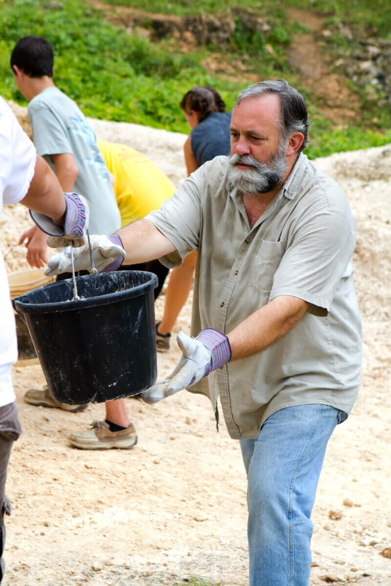 Man helps pass along a bucket of dirt to a fellow missionary on a trip to build a church in Jamaica.
